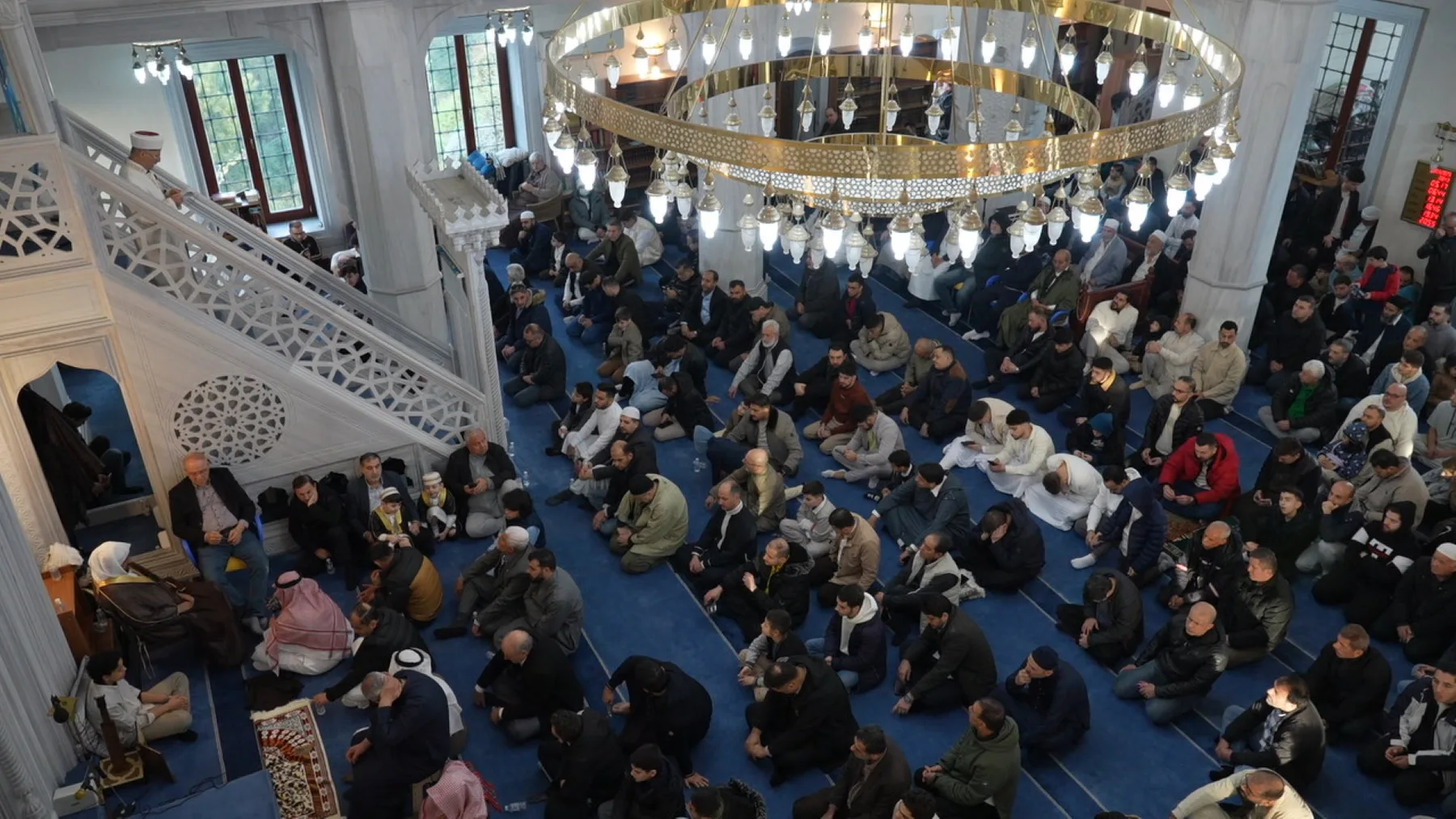 Jumu‘ah fills the main floor, the balcony and the entrance hall: about a thousand people, in a mosque whose main hall was built for 600. The khutbah is in Turkish, carried live into other languages for anyone who needs it.